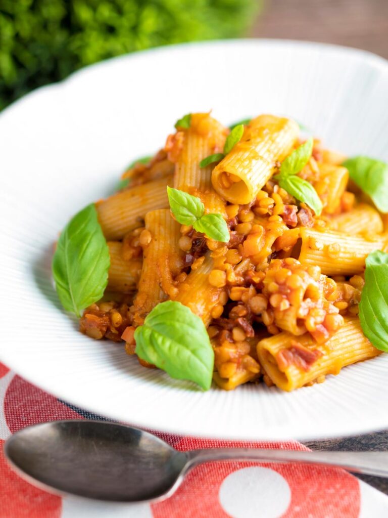 Red lentil ragu or bolognese served with rigatoni pasta with fresh basil leaves.