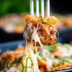 Meatball being removed from a cheesy meatball pasta bake with a fork.