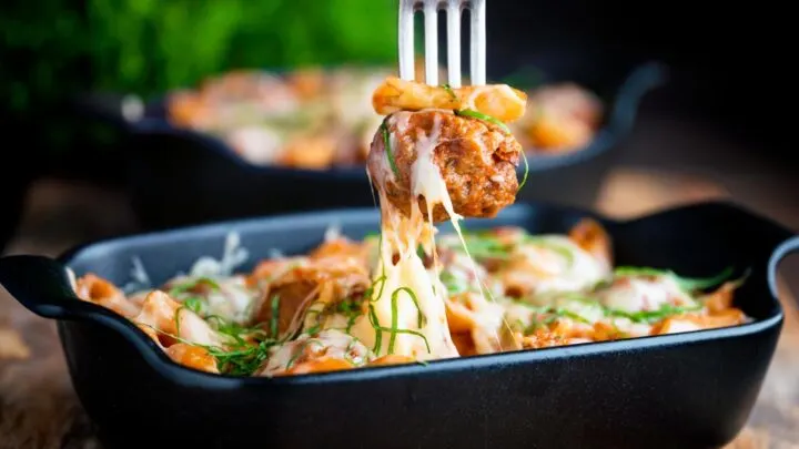 Meatball being removed from an individual cheesy meatball pasta with a fork.