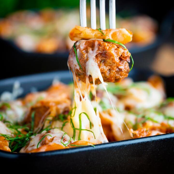 Close up of a meatball being removed from an individual cheesy meatball pasta with a fork.