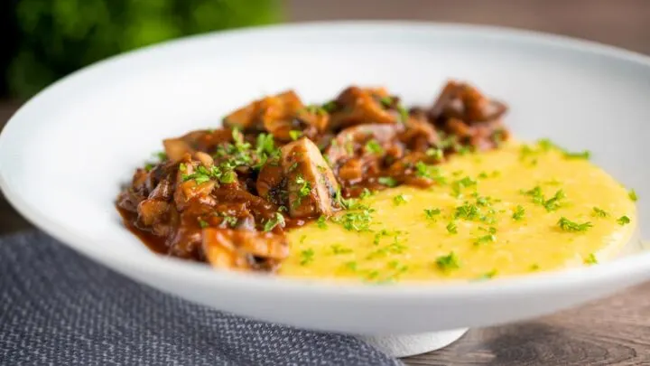 Vegan mushroom ragu served with polenta and a parsley garnish served in a white bowl.