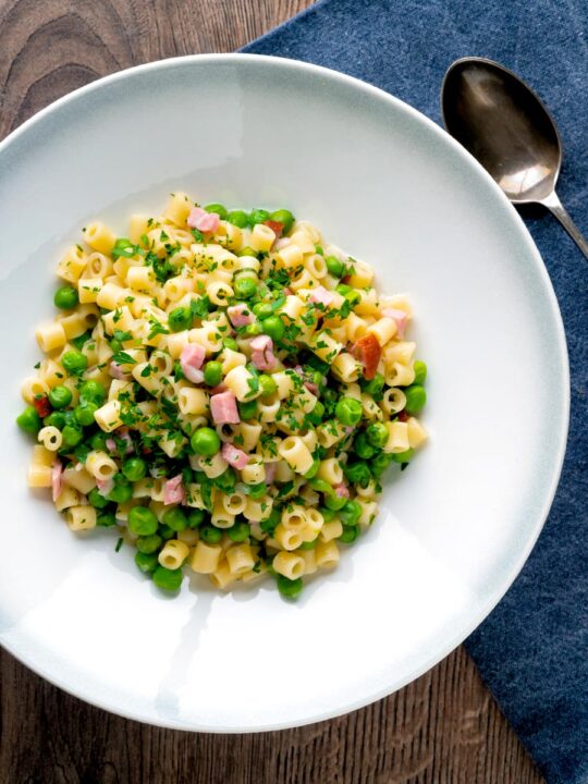 Pasta e piselli or pasta with peas and ham served in a white bowl.