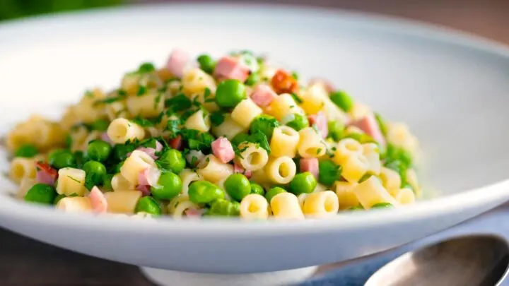 Pasta e piselli or pasta with peas and ham served in a white bowl with parsley.