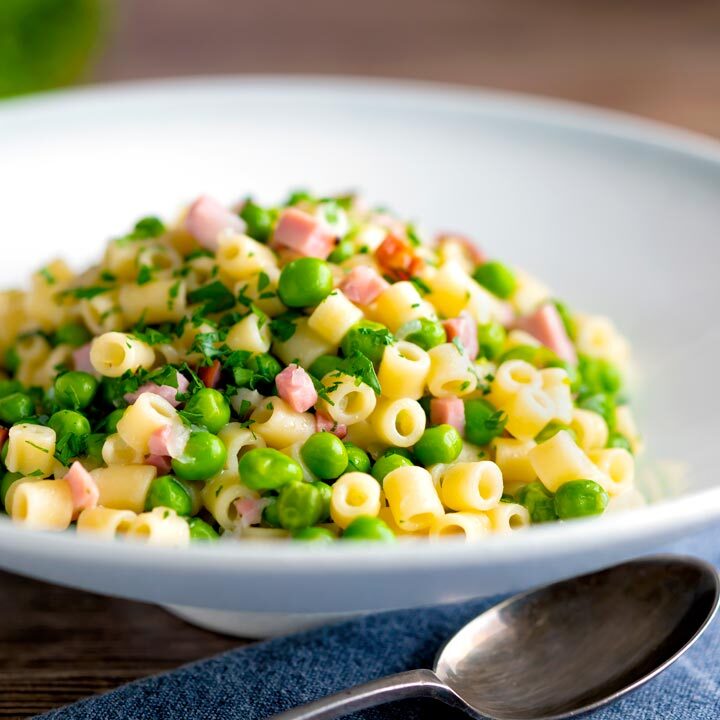 Pasta e piselli or pasta with peas and ham served in a white bowl.