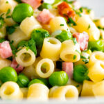 Pasta e piselli or pasta with peas and ham garnished with chopped parsley featuring a title overlay.