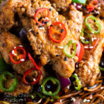 Close up salt and chilli chicken served with peppers and onion on soy sauce noodles with a title overlay.