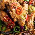 Close up salt and chilli chicken served with peppers and onion on soy sauce noodles with a title overlay.