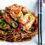 Close up salt and chilli chicken served with peppers and onion on soy sauce noodles.