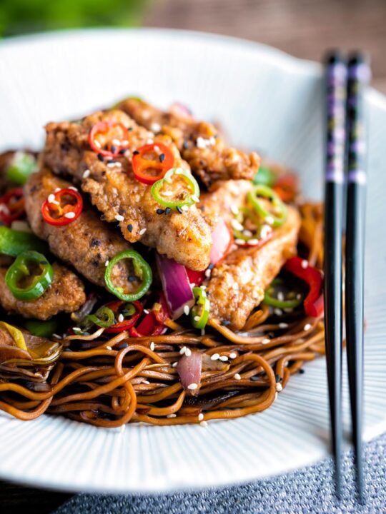 Close up salt and chilli chicken served with peppers and onion on soy sauce noodles.