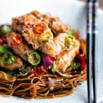 Salt and chilli chicken served with peppers and onion on soy sauce noodles with a title overlay.