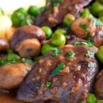 Close up chicken liver stew with button mushrooms and peas in red wine sauce.