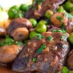 Close up chicken liver stew with button mushrooms and peas in red wine sauce.