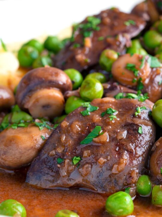 Close up chicken liver stew with button mushrooms and peas in red wine sauce.