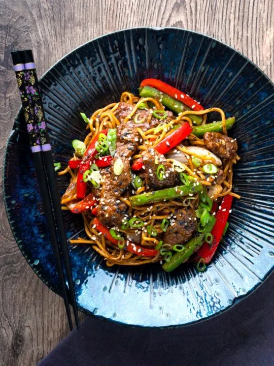 Overhead Szechuan beef stir fry with noodles and bell peppers served in a blue bowl