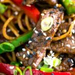 Close up Szechuan beef stir fry with noodles and bell peppers.