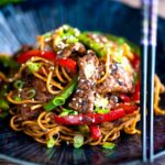 Szechuan beef stir fry with noodles and bell peppers served in a blue bowl.