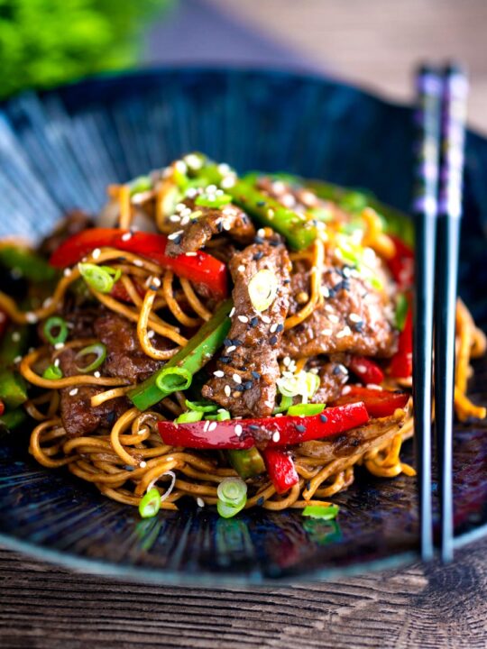 Szechuan beef stir fry with noodles and bell peppers served in a blue bowl.