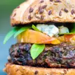 A venison burger served on a bun topped with blue cheese, gin cooked peaches & basil.