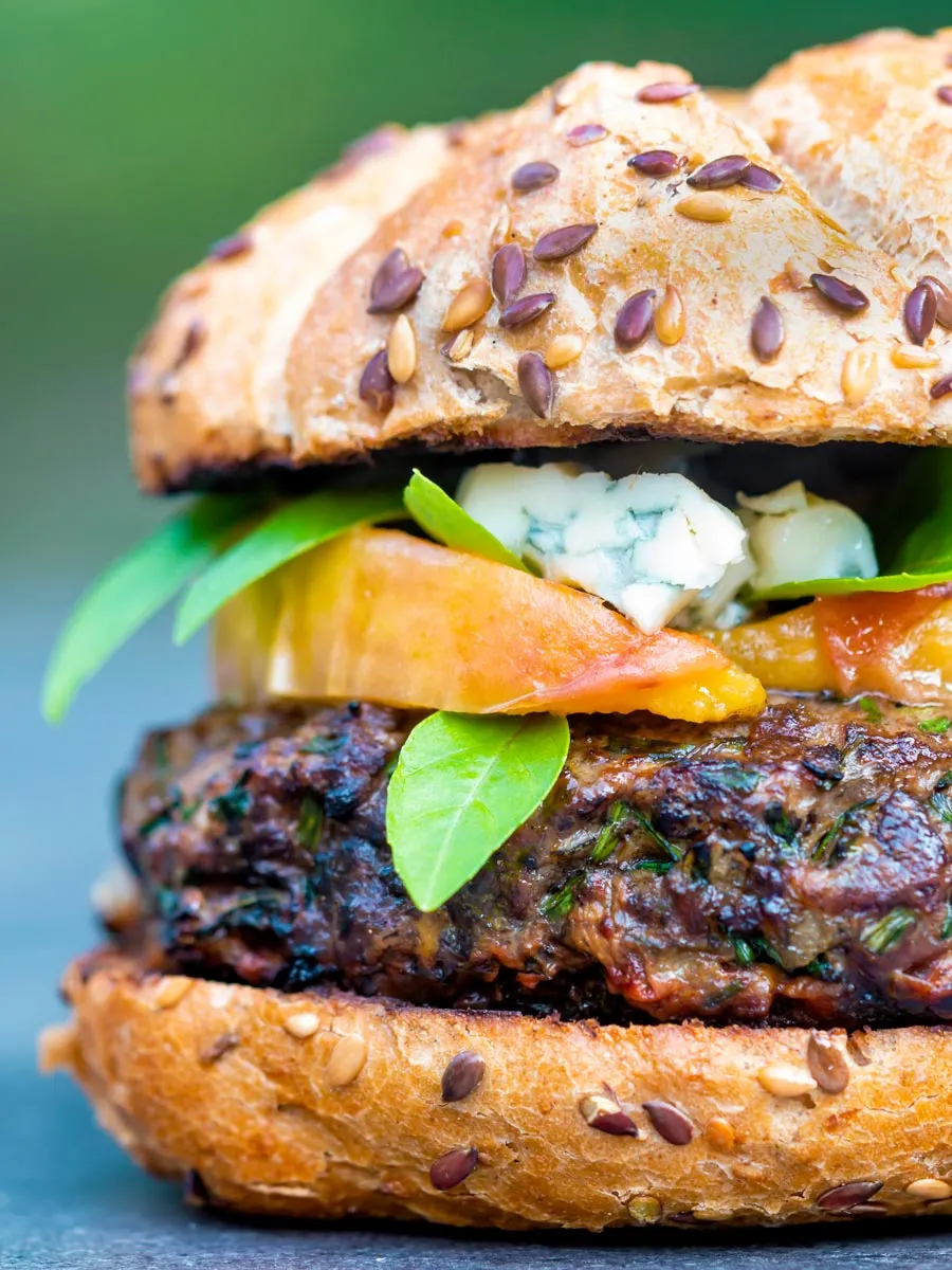 A venison burger served on a bun topped with blue cheese, gin cooked peaches & basil.