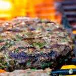 Venison burgers being cooked on a flaming barbecue.