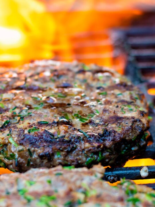 Venison burgers being cooked on a flaming barbecue.