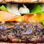 Close up venison burger served on a bun topped with blue cheese, peaches & basil.