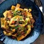 Overhead rich venison ragu sauce served with pappardelle pasta in a blue bowl.