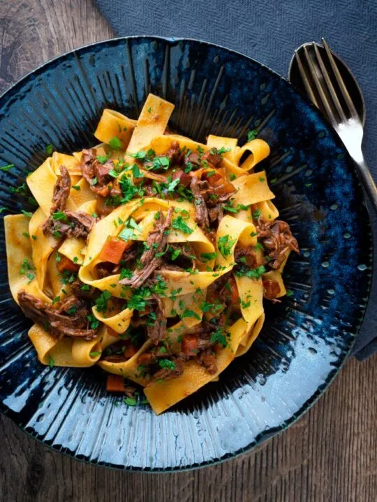 Overhead rich venison ragu sauce served with pappardelle pasta in a blue bowl.