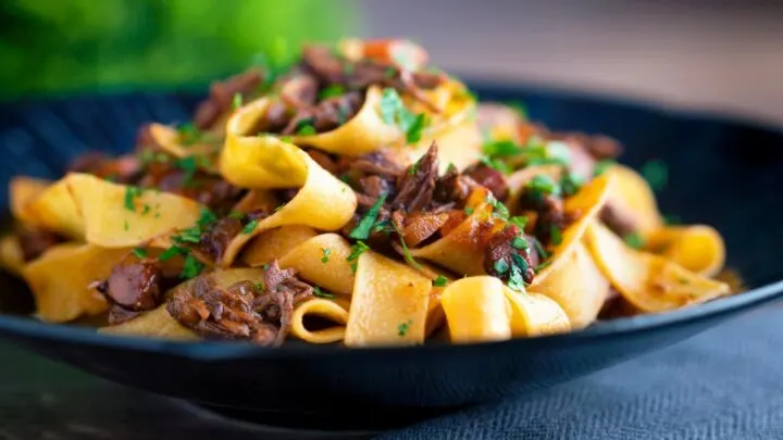 Shredded venison ragu sauce served with pappardelle pasta in a blue bowl.