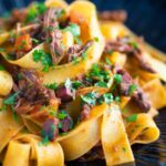 Venison ragu sauce served with pappardelle pasta in a blue bowl.