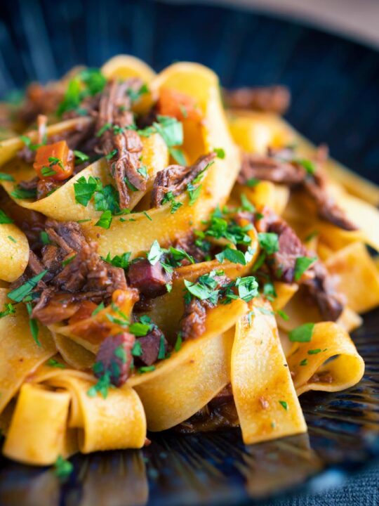 Venison ragu sauce served with pappardelle pasta in a blue bowl.