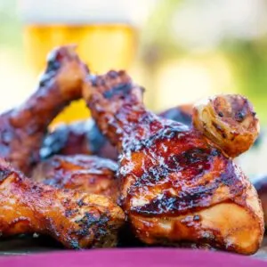Grilled BBQ chicken drumsticks with a beer, paprika and honey glaze with a beer in the background.