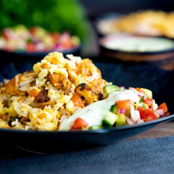 Spicy chicken tikka biryani served in a blue bowl with kachumber salad and mint raita.