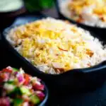 Chicken tikka biryani served in stoneware bowls with kachumber salad and raita.