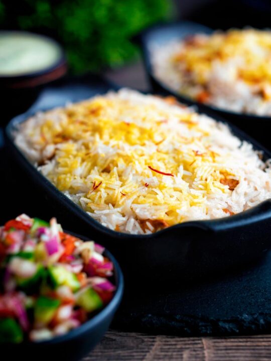 Chicken tikka biryani served in stoneware bowls with kachumber salad and raita.