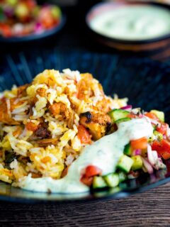 Chicken tikka biryani served in a bowl with kachumber salad and mint raita.