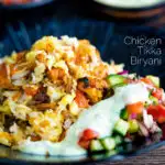 Chicken tikka biryani served in a bowl with kachumber salad and mint raita featuring a title overlay.