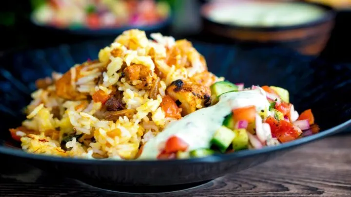 Chicken tikka biryani served in a blue bowl with kachumber salad and mint raita.