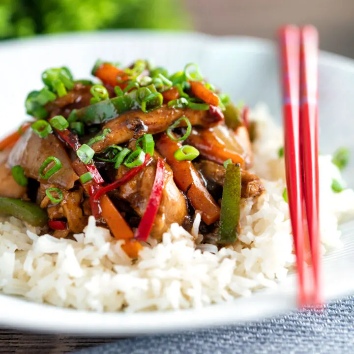 Chinese chicken with black bean sauce serve in a white bowl with rice and spring onions.