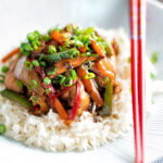 Chinese chicken with black bean sauce serve in a white bowl with rice and red chopsticks.