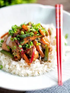 Chinese chicken with black bean sauce serve in a white bowl with rice and red chopsticks.
