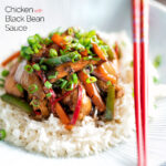 Chinese chicken with black bean sauce serve in a white bowl with rice and red chopsticks featuring a title overlay.