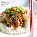 Chinese chicken with black bean sauce serve in a white bowl with rice and red chopsticks featuring a title overlay.