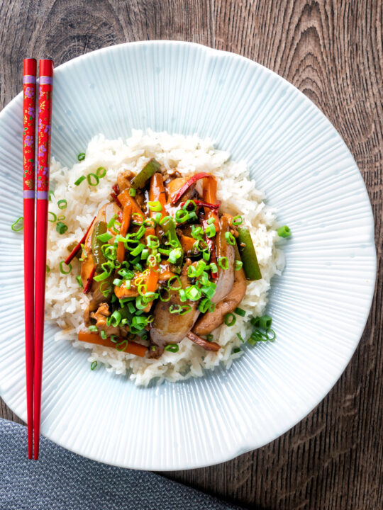 Overhead Chinese chicken with black bean sauce serve in a white bowl with rice.