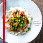 Overhead Chinese chicken with black bean sauce serve in a white bowl with rice featuring a title overlay.