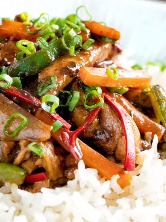 Close up Chinese chicken with black bean sauce serve in a white bowl with rice.