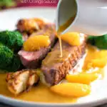 Orange sauce being poured over a rosy pan fried duck breast with crispy skin featuring a title overlay.