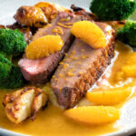 Pan fried duck breast with orange sauce served with roast potatoes & broccoli featuring a title overlay.