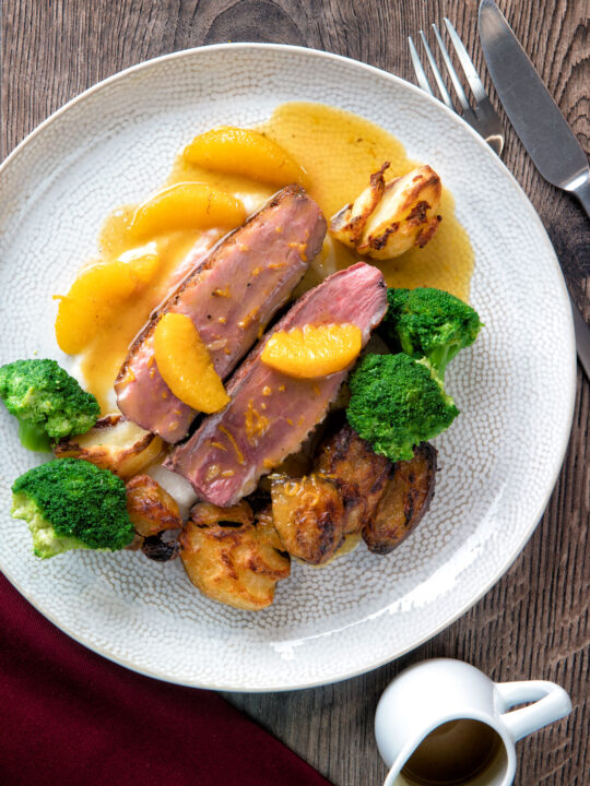 Over head pan fried duck breast with orange sauce served with roast potatoes.