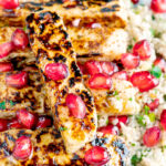 Close up halloumi cheese salad with pomegranate arils and couscous featuring a title overlay.